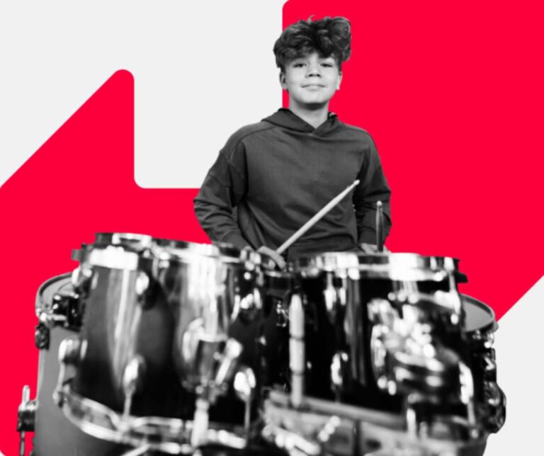 A young person sitting at a drumkit, with drum sticks in their hands